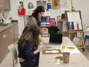 New art teacher, Mrs. Foster helps a student touch up her artwork.
