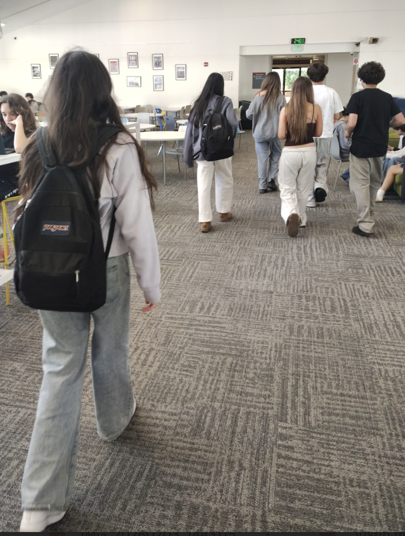 Two students both walking in the hall with the same exact backpack. 